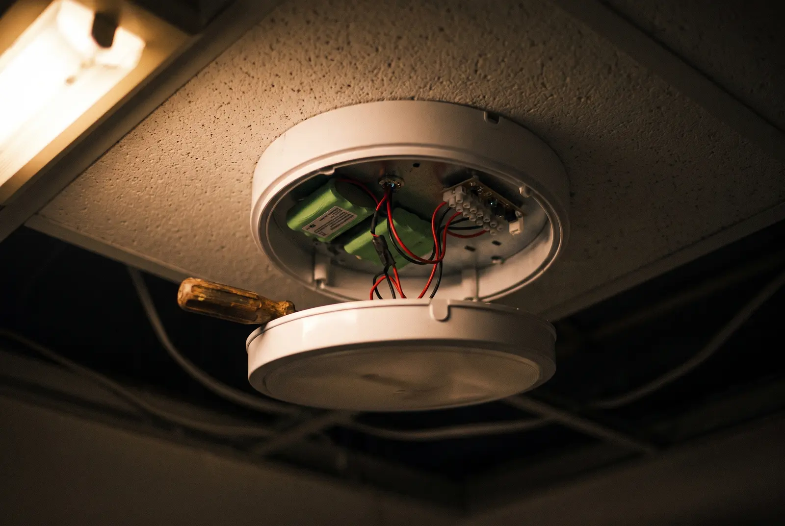An emergency lighting bulkhead with its diffuser removed, battery pack visible
