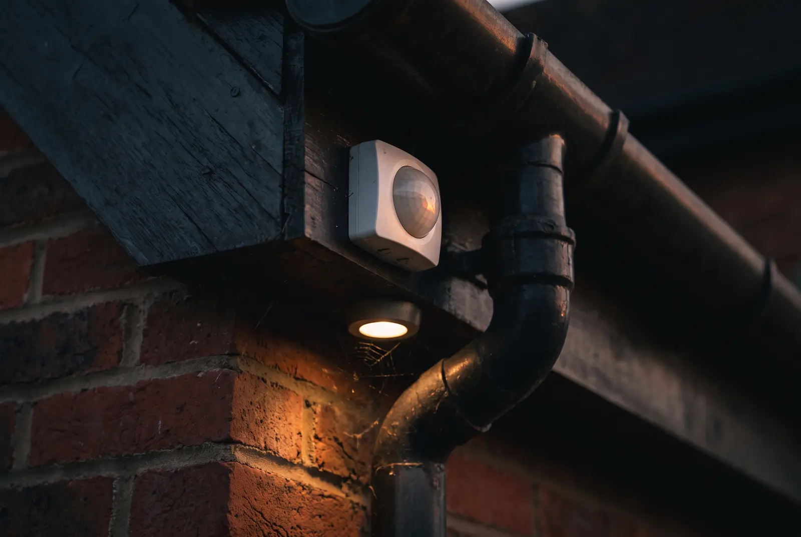 A PIR motion sensor mounted under the eaves of a house at dusk