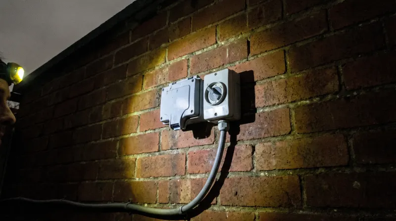 A weatherproof outdoor socket and isolator on a garage wall, found by an emergency electrician in Loughton