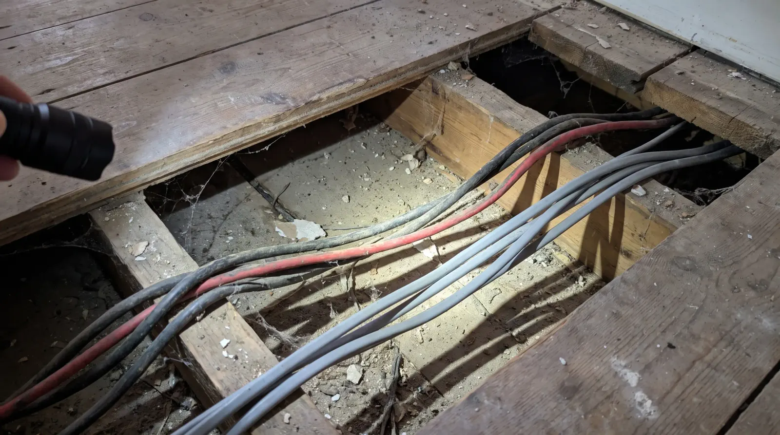 Old rubber-sheathed and newer cable running together under lifted floorboards — house rewire in Dagenham