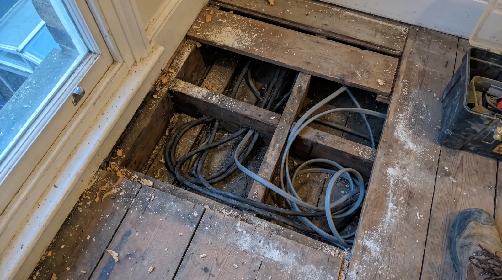 Old rubber-sheathed and newer cable running together under lifted floorboards — house rewire in Gants Hill