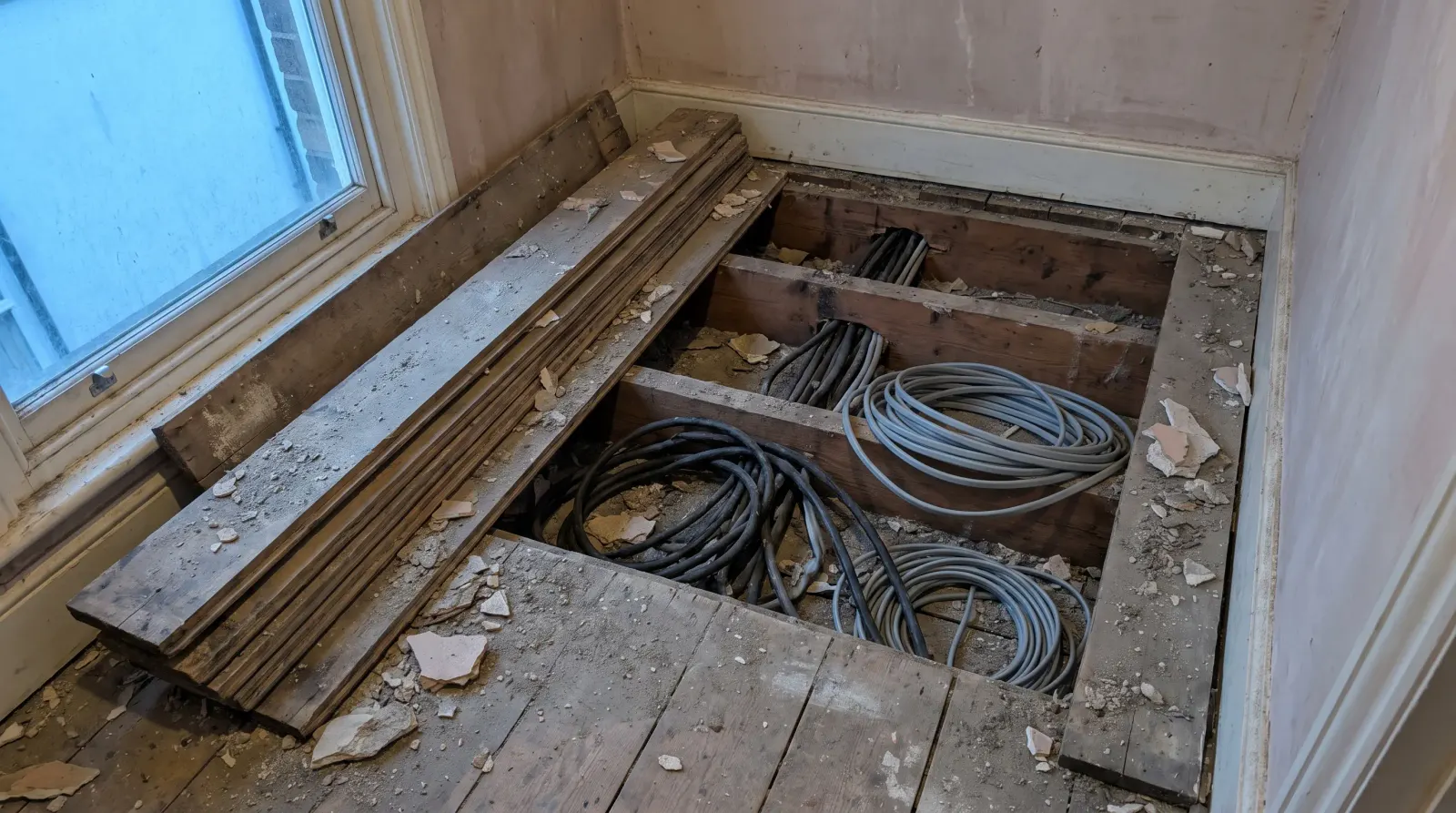 Old rubber-sheathed and newer cable running together under lifted floorboards — the kind of house rewire an electrician in Hornchurch is called out for