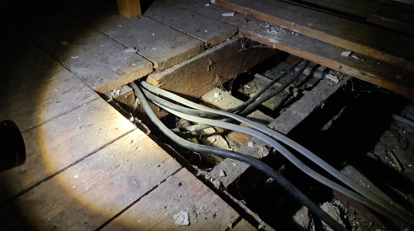Old rubber-sheathed and newer cable running together under lifted floorboards — the kind of house rewire an electrician in Sidcup is called out for