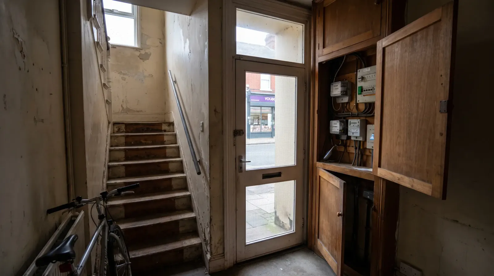 A stairwell to flats above a shop with the meter cupboard open — the kind of landlord electrics an electrician in Barking is called out for