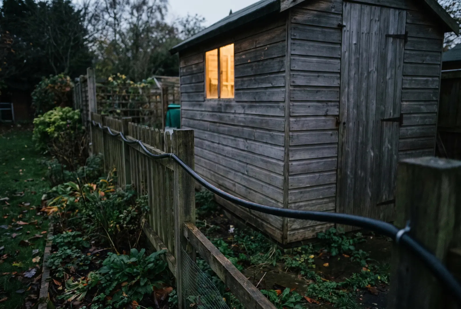 A garden outbuilding lit at dusk with armoured cable run to it