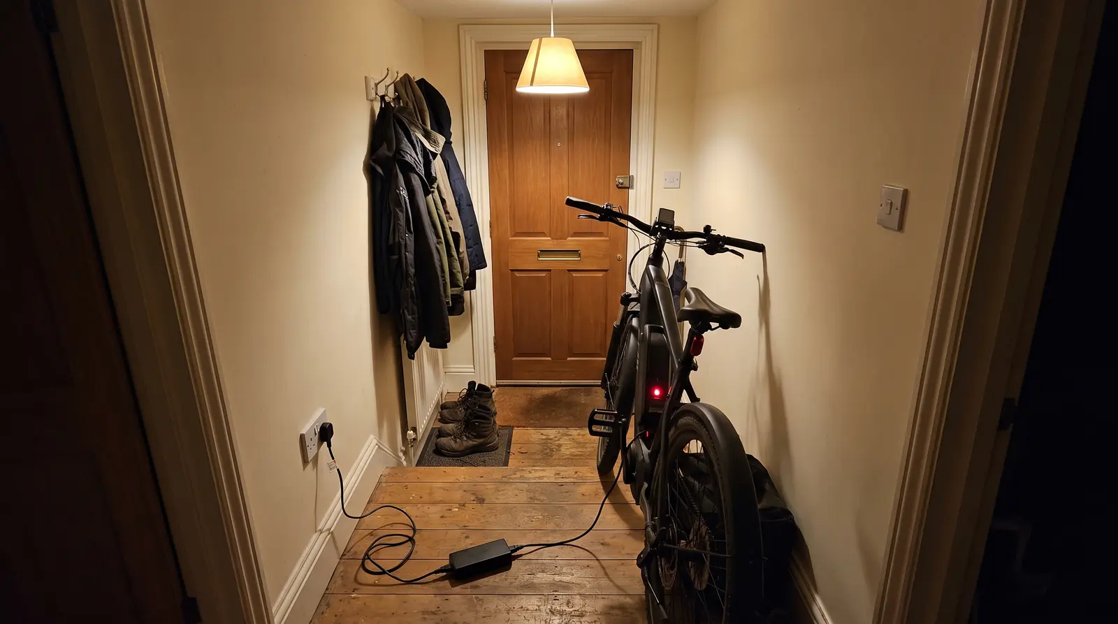 An electric bicycle on charge in a narrow hallway directly beside the front door