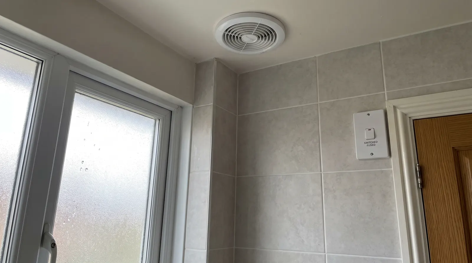 A switched fused connection unit fitted on a bathroom wall beside an extractor fan