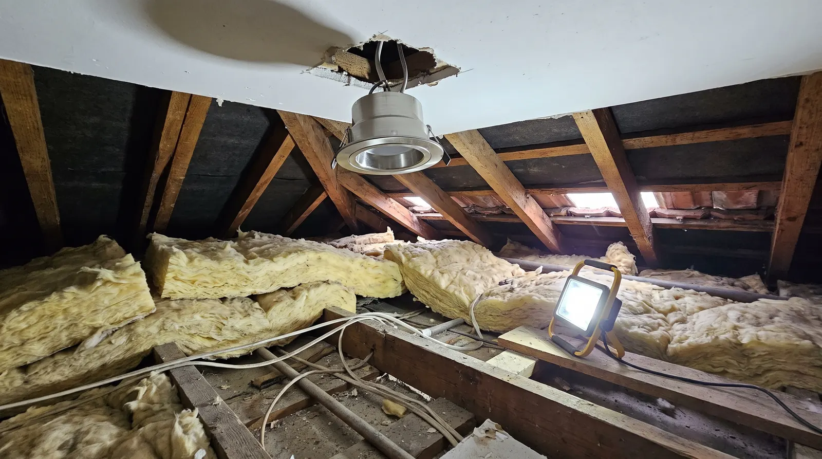 A downlight housing protruding through a ceiling in a loft, with insulation kept clear around it