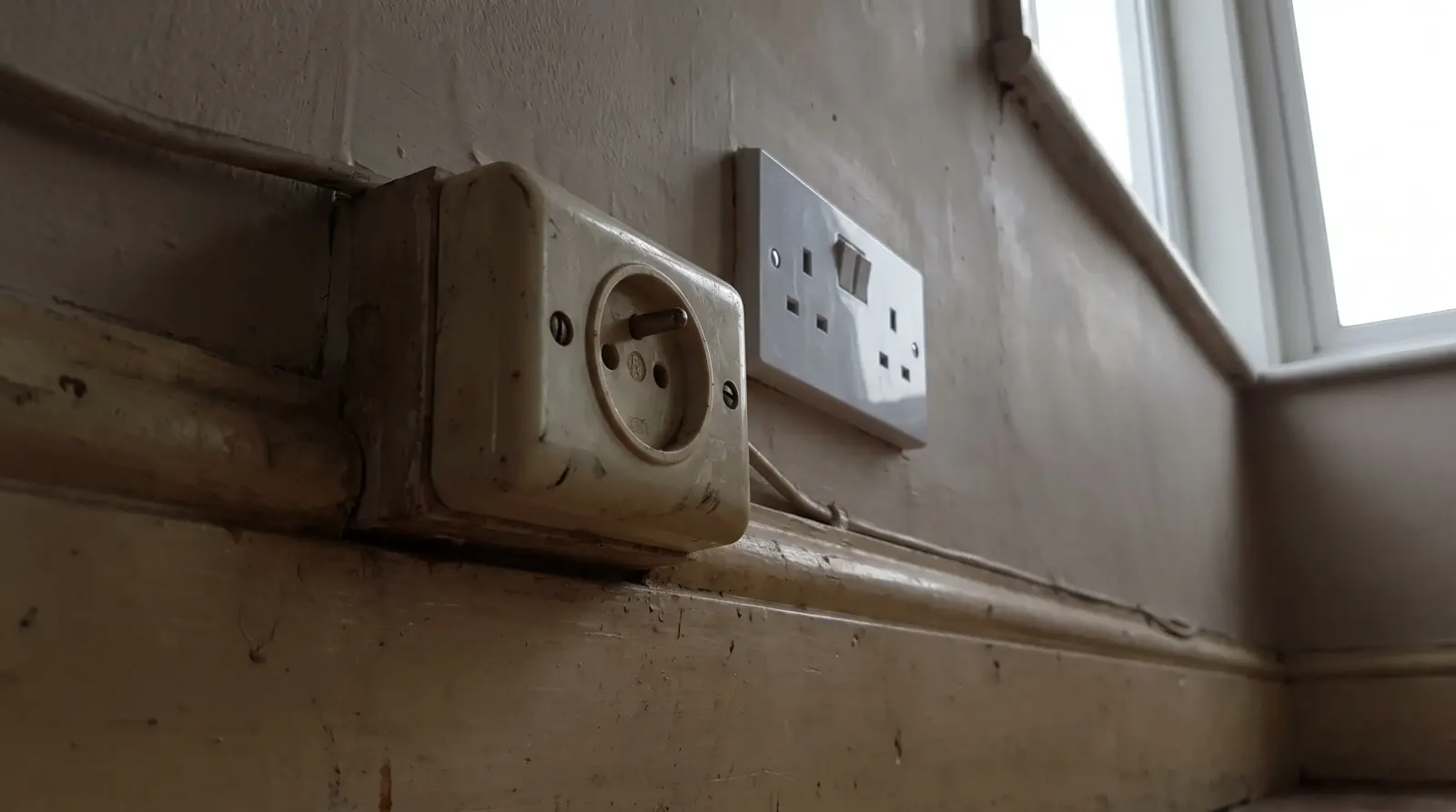 A surviving round-pin socket next to a modern three-pin one — new sockets in Chadwell Heath