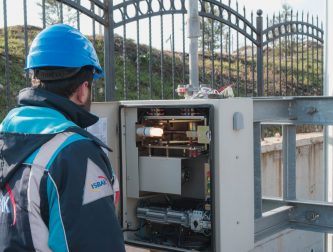 Electrician wearing a hard hat inspecting an outdoor fuse box during an EICR safety inspection