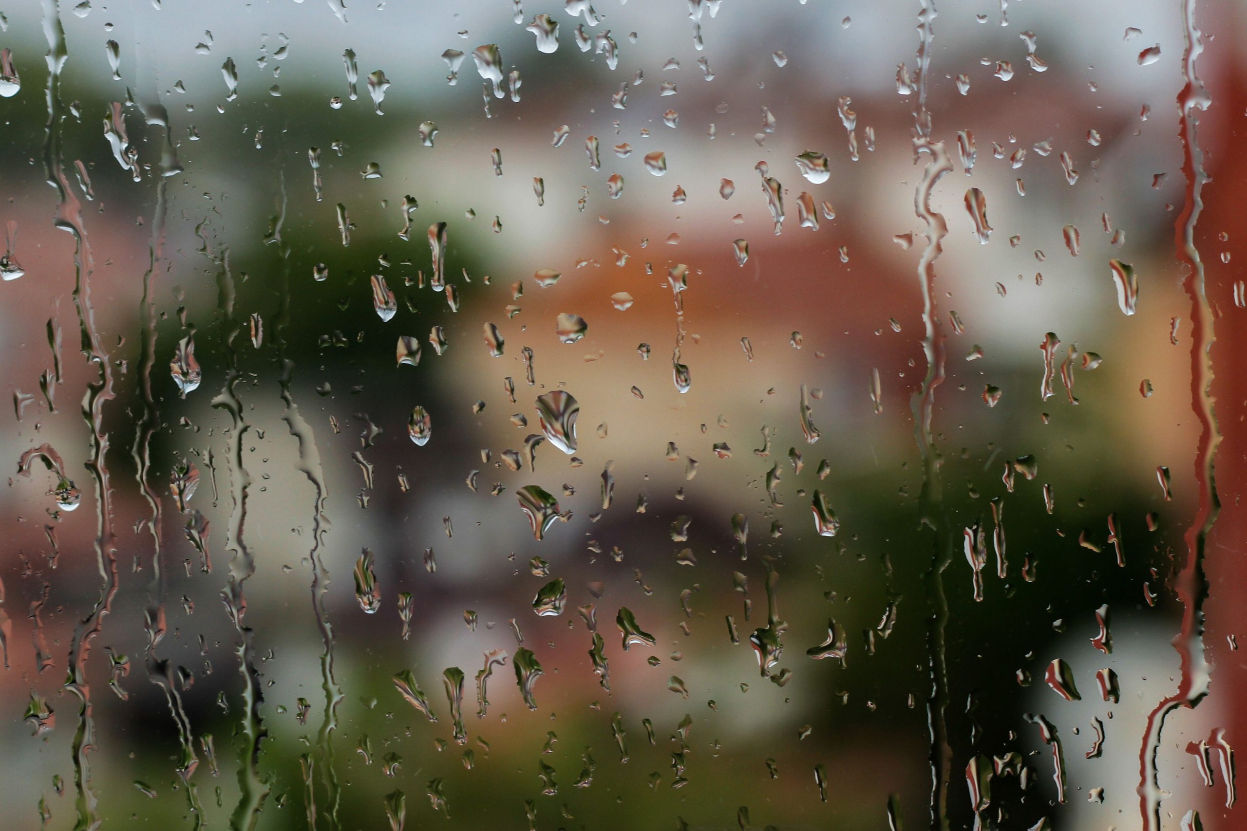 Rain streaming down a window with blurred houses outside during a storm